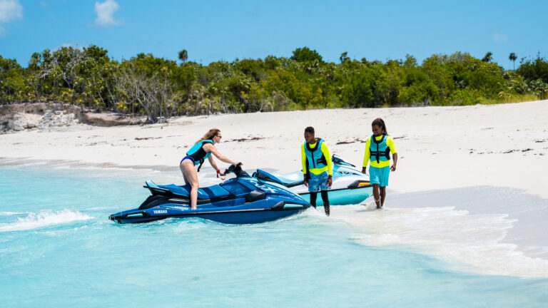 Guides helping a guest onto a jet ski at a white sand beach
